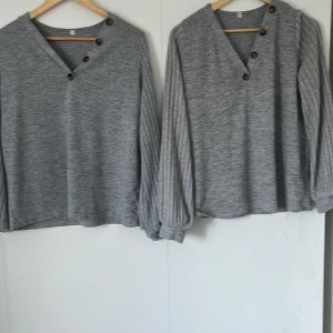  2 st Grå tröja med knappar och v-ringning - Snygga tröjor  med v-ringning och dekorativa knappar längs halsen. Tröjan har långa ärmar och en avslappnad passform. Perfekt för dig som gillar en enkel men ändå stilren look.