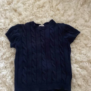 Mörkblå stickad tröja Gina Tricot - Mörkblå stickad tröja från Gina Tricot med korta ärmar och klassiskt flätmönster. Tröjan har rund halsringning och ribbade kanter, perfekt för dig som gillar en enkel men snygg look. Passar till både jeans och kjol.