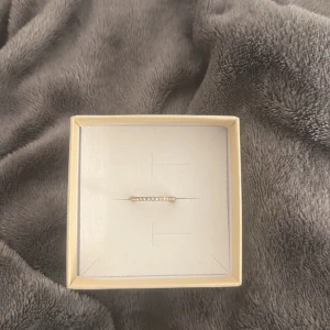 Ring Mockberg - Superfin tunn guldfärgad ring från Mockberg, dekorerad med små gnistrande stenar runt hela ringen. Perfekt för dig som gillar stilrena och eleganta smycken med lite extra bling. Kommer i original ask. 