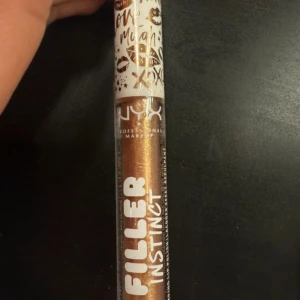 NYX Filler Instinct Brunch Drunk - NYX Filler Instinct läppglans i nyansen Brunch Drunk. Glanset har en skimrande, guldig-bronsig färg och kommer i en smidig tub med vit kork dekorerad med guldiga läppar och text. Perfekt för att ge läpparna extra volym och glans.