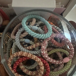 Färgglada flätade armband i tyg - Säljer flera flätade armband i olika färger som ljusblå, rosa, grön, beige och röd. Armbanden är gjorda av mjukt tygmaterial och har små plastdetaljer. Perfekta för att mixa och matcha till din stil!