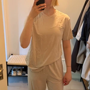 Beige mjukis/pyjamas t-shirt från SKIMS - Säljer en beige t-shirt från SKIMS i mjuk och stretchig modal- och bomullsblandning. T-shirten har klassisk passform, rund halsringning och korta ärmar. Perfekt basic-plagg. Superbekväm.