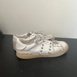 Valentino garavani vita sneakers - Viktigt: På tredje bilden ser man att dom är lite slitna på sidan men det är inget som inte går att laga! Vita sneakers från valentino garavani  med ikoniska gulfärgade nitar längs sidor. 
