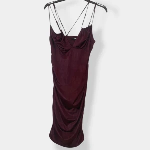 Vinröd långklänning från Bik Bok - Supersnygg vinröd långklänning från Bik Bok med tunna axelband och draperad front. Klänningen har en elegant v-ringning och åtsittande passform som framhäver siluetten. Perfekt för dig som vill sticka ut med en stilren look.