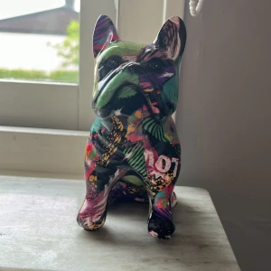 Prydnad hund - Bilderna visar en färgglad bulldog-skulptur i popkonst-stil, täckt av graffiti-liknande mönster och ordet 'LOVE'. Det är ingen bok på bilderna.