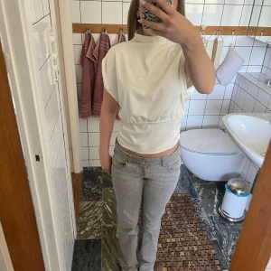 Vit topp/blus från Selma Omari x NA-KD - Säljer en stilren vit top/blus från Selma Omari x NA-KD. Toppen har hög krage, korta ärmar och markerad midja. Den är helt ny, säljer den för att den är lite för stor för mig. 