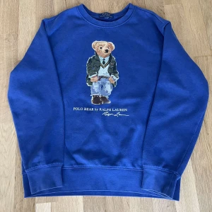 Blå Polo Bear tröja från Ralph Lauren - Blå långärmad tröja från Ralph Lauren med ikoniska Polo Bear-trycket framtill. Rund halsringning och mjukt material i bomull. Perfekt för dig som gillar klassisk streetstyle med en twist. Snygg att matcha med jeans eller cargobyxor. Den passar en person som är runt 165 cm lång och har en normal kroppsbyggnad. Plagget passar perfekt till lite blåsiga sommardagar och kyliga sommarkvällar. Plagget kostar ca 1600 kronor nypris. Tröjan är andvänd ca 5 gånger. Pris går ej att diskuteras. Skick 9/10