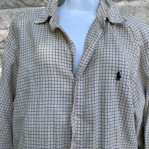 Rutig skjorta från Ralph Lauren XL - Riktigt snygg rutig skjorta från Ralph Lauren i klassisk fit. Skjortan är vit med gula och svarta rutor, har lång ärm och knappar framtill. Broderad logga på bröstet och tillverkad i 100% bomull. Perfekt för dig som gillar stilren och tidlös design.