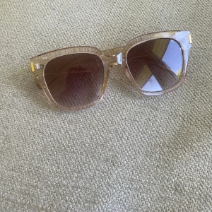 Beige fyrkantiga solglasögon - Stilrena solglasögon med transparent brun plastbåge och fyrkantig form. Glasen är bruna och ger en cool vintagekänsla. Perfekta för att lyfta din look med en touch av retro.