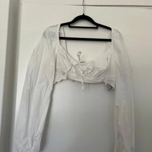 Vit croppad blus med puffärm - Superfin vit croppad blus med långa puffärmar och söt knytning framtill. Viss missfärgning under armar efter deo men inget som syns vid användning, se bild.