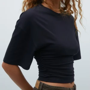 Mörkblå croppad topp från Gina Tricot - Säljer en mörkblå croppad topp från Gina Tricot med korta ärmar och snygg rynkdetalj i sidorna. Aldrig använt helt ny!