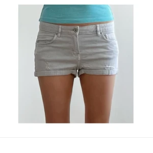 Ljusgråa jeansshorts med upprullad kant - Snygga ljusgråa jeansshorts med upprullad kant och klassisk femficksdesign. Shortsen har låg midja och en liten sliten detalj framtill för en avslappnad look. Perfekta för varma dagar och enkel att matcha med allt.