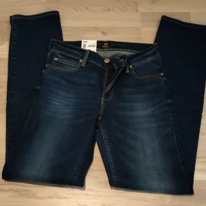 Lee Classic Straight jeans mörkblå - Mörkblå jeans från Lee i modellen Classic Straight. Snygg tvätt med lätt slitning framtill, raka ben och klassiska fem fickor. Gula kontrastsömmar och läderpatch bak i midjan. Perfekta jeans för dig som gillar en tidlös look.