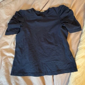 Mörkblå T-shirt med puffärmar - Supersnygg mörkblå T-shirt med korta puffärmar och rund halsringning. Perfekt för dig som vill ha en enkel men ändå trendig look med extra volym på axlarna.