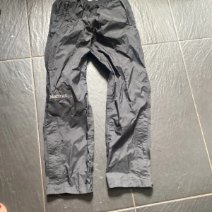 Regnbyxor 146/152 Marmot - Ett par sällan använda regnbyxor märket Marmot. Med både blixtlås och knappar vid fotleden. 