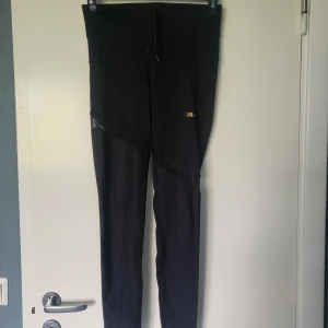 Svarta träningstights från Casall - Säljer ett par svarta träningstights från Casall med diskreta meshdetaljer och reflekterande inslag på benen. Tightsen har en tight passform och dragsko i midjan. Perfekta för gymmet eller löprundan! Storlek 36, använda ett fåtal gånger. 