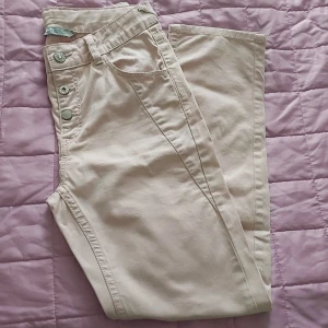 Rosa byxor med knappar, storlek 11-12 år  - Snygga rosa byxor i storlek 11-12år med flera knappar framtill och klassiska fickor. Byxorna har en rak passform och är tillverkade i ett mjukt bomullsmaterial. Perfekta för en stilren och avslappnad look.