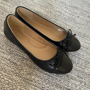 Svarta ballerinaskor med rosett - Säljer ett par klassiska svarta ballerinaskor med rund tå och söt rosettdetalj framtill. Använda en gång