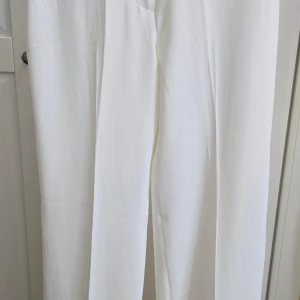Vita kostymbyxor med rak passform - Säljer ett par klassiska vita kostymbyxor med rak passform. Byxorna har pressveck framtill och är perfekta för en stilren look. De är midjehöga och har en enkel design utan synliga detaljer.