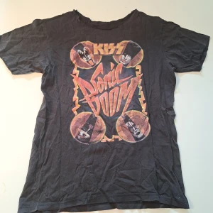 Svart KISS Sonic Boom Tour t-shirt - Cool svart t-shirt med färgglatt tryck från KISS Sonic Boom Tour 2010. Framsidan har bandets logga och medlemmarnas ansikten, baksidan visar turnédatum och städer. Perfekt om du gillar bandet.