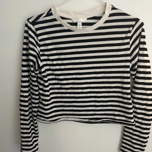 Svartvit randig croppad tröja från H&M - Tröjan har långa ärmar och rund halsringning med vit kant.