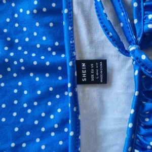 Blå prickig klänning från SHEIN - Säljer en blå klänning från SHEIN med vita prickar och korta puffärmar. Klänningen har en söt knytning upptill och en rak passform som faller fint. Perfekt för sommarens alla tillfällen!