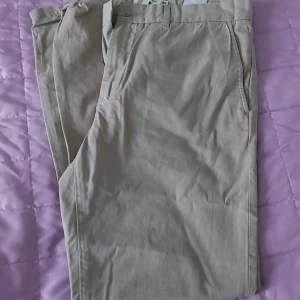 Beige chinos från H&M - Snygga beige chinos från H&M med klassisk passform och bälteshällor. Byxorna har snedställda fickor fram och är tillverkade i mjuk bomull, perfekta för en stilren look.