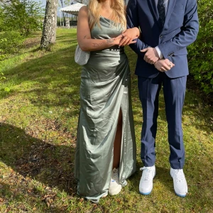 Grön satinklänning med slits och oneshoulder - Säljer en elegant lång grön satinklänning med oneshoulder och hög slits framtill. Klänningen har en snygg drapering över bysten och en figurnära passform. Perfekt för bal eller fest! 💚 Använd en gång och är nytvättad. Jag är 160 lång🌸Nypris 3900kr