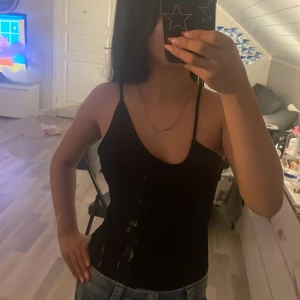 Svart body med smala axelband - Säljer en svart body med smala axelband och djup urringning. Perfekt för varma dagar eller som lager under andra plagg. Enkel och stilren design som passar till mycket.