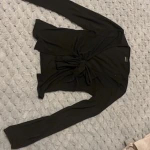 Svart långärmad topp med knyt från Gina Tricot - Svart långärmad topp från Gina Tricot med snygg knytdetalj framtill. Perfekt att styla med jeans eller kjol för en trendig look. Mjuk och skön bomullskänsla.