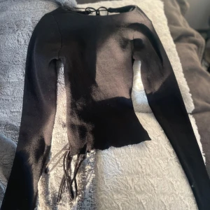 Svart ribbad topp med snörning i ryggen - Säljer en svart långärmad ribbad topp med snygg snörning i ryggen och croppad passform. Den är även väldigt stretchig, aldrig använd bara testad.