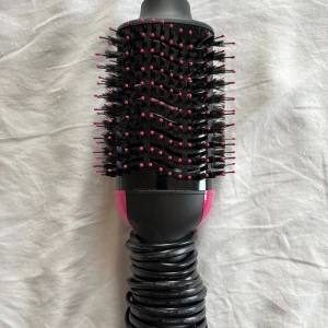 Revlon varmluftsborste  - Säljer en Revlon varmluftsborste i svart med rosa detaljer. Borsten har ovala borsthuvuden med svarta borst och rosa toppar, perfekt för att styla och ge volym till håret. Ergonomiskt handtag och lång sladd för enkel användning.