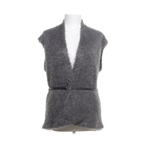 Grå pälsväst med bälte från Gina Benotti - Mysig grå pälsväst från Gina Benotti med v-ringning och ett smalt svart bälte i midjan. Västen har en fluffig textur och är perfekt för lager-på-lager-stil. Passar dig som gillar att sticka ut med en unik och trendig look.