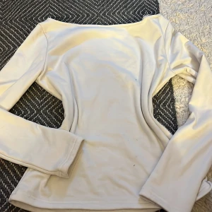 Vit långärmad topp med bred hals - Säljer en stilren vit långärmad topp med bred, något båtformad halsringning. Mjuk och stretchig i materialet, perfekt för en clean och enkel look. Passar dig som gillar minimalistisk stil.