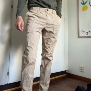 Beiga chinos från Michael Kors - Säljer ett par beiga chinos från Michael Kors i slim fit-modell. Byxorna har klassisk passform med snedställda fickor fram och är tillverkade i ett mjukt bomullsmaterial. Perfekta för en stilren och avslappnad look.
