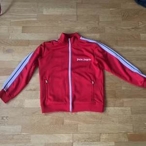 Röd track jacket från Palm Angels - Tjena! Säljer en röd palm angels zip. Ärmarna har blivit lite rosa under tvätten men i övrigt fint skick. Tröjan är storlek S. Det är bara att kontakta om ni undrar något😁priset kan även diskuteras!