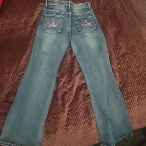 Blå bootcut jeans med broderade bakfickor - Säljer ett par blå bootcut jeans med snygga broderade kronor på bakfickorna. Är i storlek S och skulle passa perfekt en som gillar dramatiska byxor! Säljer eftersom att det inte kommer i användning.