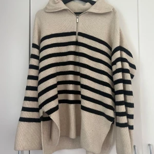 Beige och svart randig stickad tröja med dragkedja - Säljer en oversized stickad tröja i beige med svarta ränder och dragkedja framtill. Tröjan har långa vida ärmar och en krage, perfekt för lager-på-lager. Supermjuk och skön att ha på sig. Från Hm i stolen M