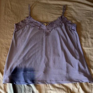 Mörkblå linnetopp med spets från Amisu - Säljer en mörkblå linnetopp från Amisu med tunna axelband och vacker spetsdetalj upptill. Toppen har en mjuk och följsam känsla, perfekt för att skapa en stilren look.
