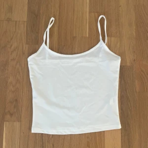 Vit linnetopp med smala axelband - Säljer en enkel och stilren vit linnetopp med smala axelband. Perfekt att matcha med jeans eller kjol för en fräsch look. Toppen har rak passform och är tillverkad i ett mjukt material.