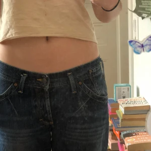  Mörkblå ankellånga jeans med knappar - Klassiskt mörkblå jeans med raka ben och knäppning med knappar. Jeansen har fem fickor och en något lösare passform. Snygga slitningar och detaljer i gul söm. Perfekta för en avslappnad stil. De är Baggy och lågmidjade men inte så stretchiga. Köpte secondhand och lappen med storlek är tyvärr avklippt. Det är märket Divided. 