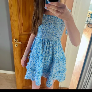 Sommar klänning  - Supersöt blå klänning med små blommor och volangdetaljer nertill. Smockad överdel och knyte vid axlarna så storleken och passform går att gystera storlek xs