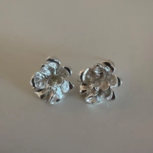 Blommiga silverfärgade örhängen - Säljer ett par fina örhängen i form av blommor i silverfärg. De har en tydlig blomdesign med flera kronblad och är perfekta för att ge en söt och stilren touch till din look.