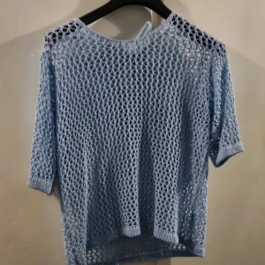 Ljusblå stickad nättröja med knyt i nacken - Säljer en ljusblå stickad nättröja med trekvartsärm och knytband i nacken. Tröjan har en luftig och öppen stickning som ger en cool och avslappnad look. Perfekt att slänga över ett linne eller bikini. 100kr