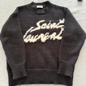 Saint Laurent tröja - Säljer en exklusiv Saint Laurent Paris tröja i storlek S. Svart med ikoniskt fluffigt Saint Laurent tryck framtill. Tillverkad i Italien i en lyxig materialmix med avslappnad passform och ribbstickade muddar. Sparsamt använd, mycket gott skick. Originaletikett medföljer fast den sitter ej fast sydd. Nypris ca 9 000 kr, mitt pris 1 199 kr. Hör av dig vid minsta fundering eller önskemål om fler bilder😊!