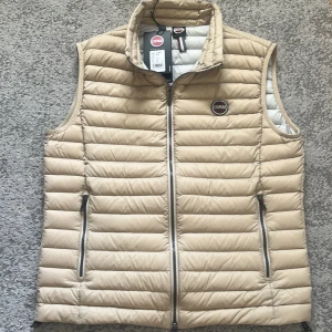 Colmar väst. HELT NY!!   M-L - Snygg beige dunväst från Colmar med quiltad design och dragkedja framtill. Västen har ståkrage och två fickor med dragkedja. Perfekt för lager-på-lager och enkel att matcha med olika outfits.