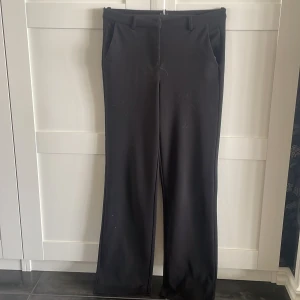 Svarta kostymbyxor med raka ben - Snygga svarta kostymbyxor med raka ben och klassiska fickor framtill. Byxorna har hällor för bälte och en stilren look som passar till många olika outfits. Materialet känns mjukt och följsamt, perfekt för dig som gillar en clean och enkel stil.