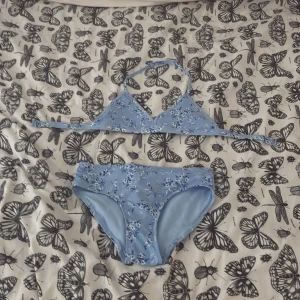 Blommig ljusblå bikini från Lindex - Supersöt ljusblå bikini från Lindex med små vita och blå blommor. Överdelen har trekantsform och knyts i nacken och ryggen. Underdelen är klassisk med samma blommiga mönster. Perfekt för strandhäng och poolparty i sommar!