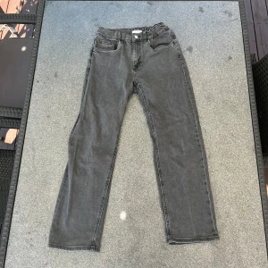 Grå raka jeans i klassisk modell - Säljer ett par grå jeans med raka ben och klassisk femficksdesign. Jeansen har normal midja och är tillverkade i mjukt denimtyg. Perfekta för dig som gillar en enkel och tidlös look. Passar till det mesta och är lätta att styla.