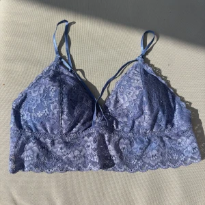 Blå spets bralette från Åhléns - Supersöt blå bralette från Åhléns i storlek M. Gjord i mjuk spets med blommigt mönster och tunna justerbara axelband. Toppen har en v-ringad form och bred spetskant nedtill för extra detalj. Perfekt att styla under en skjorta eller som den är!